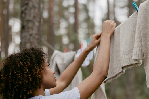 A woman hangs clean laundry on a clothesline in a forest setting, promoting natural lifestyle.